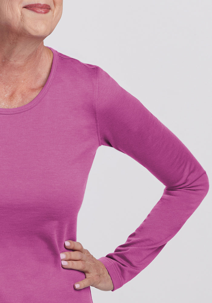 A person wears the Woolx Remi Long Sleeve T-Shirt in Purple Wine, standing with one hand on their hip and smiling. Only their lower face, upper body, and arm are visible against a plain light background.