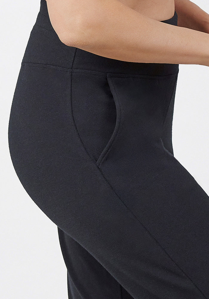 A close-up side view shows a person wearing Woolx Madden Joggers - Black, featuring a pocket, with their hip, waist, and arm visible against a plain light background.