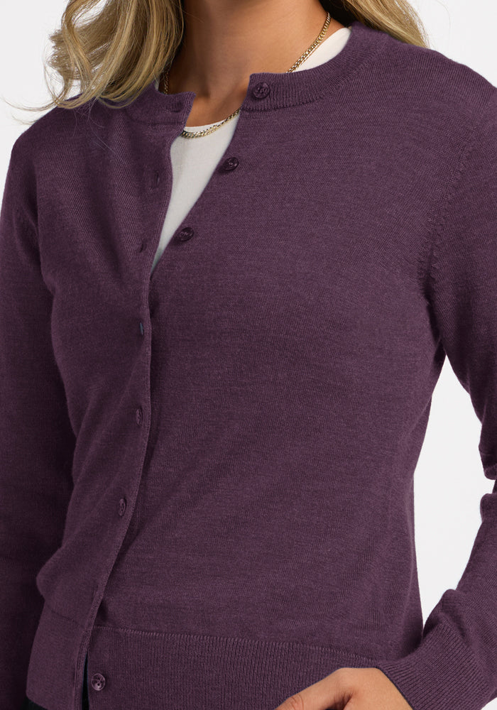Woman models the Woolx Caitlin Sweater in Purple Iris over a white top, hand on waist, against a white background.