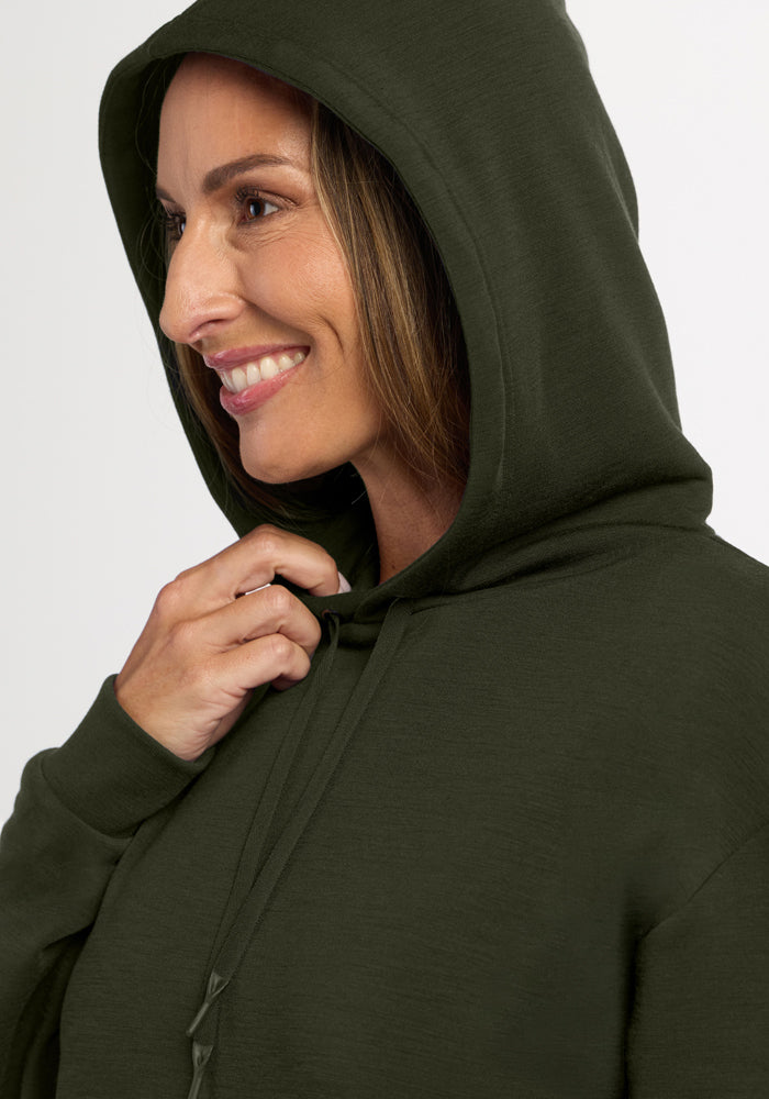 Woman smiles in the Woolx Avery Hoodie - Duffel Bag, hood up, shown from the side against a plain background.