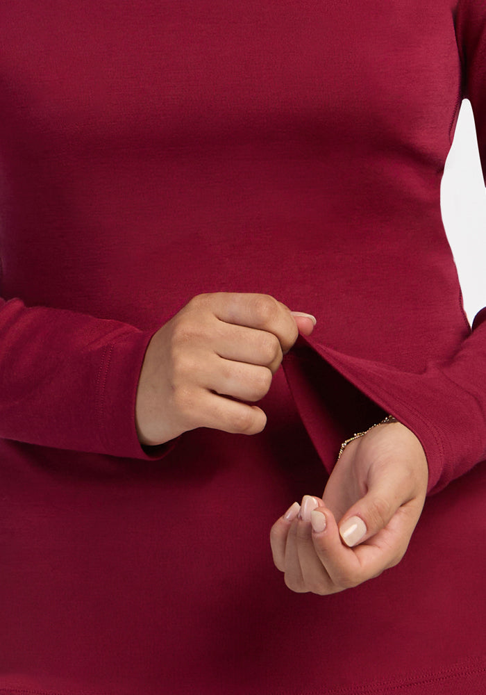 Person stretching the Woolx Brooke 1/4 Zip in Beet Red, showing its fit and Merino wool texture against white background.