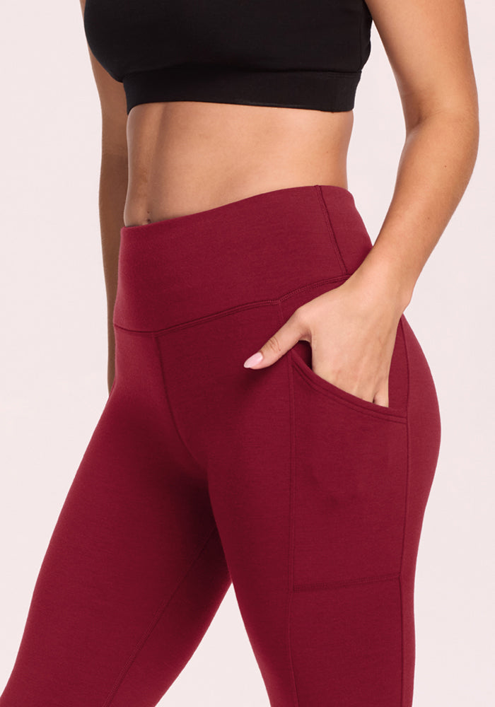 Woman in Woolx Piper Pocket Leggings - Pinot Noir and black crop top, standing with one hand in the pocket.