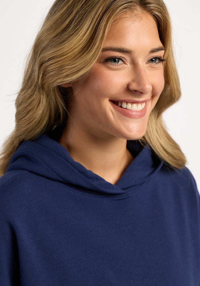 A smiling woman wearing a dark blue moisture-wicking Woolx Genevieve Hoodie - Ocean Cavern.