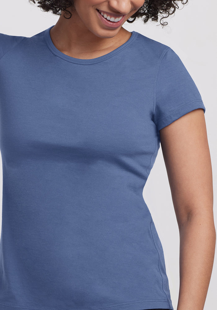 A woman wearing the Woolx Addie Crew Neck - Skyline, a fitted short-sleeved top, is smiling with her head slightly turned, showing only part of her face against a plain, light background.