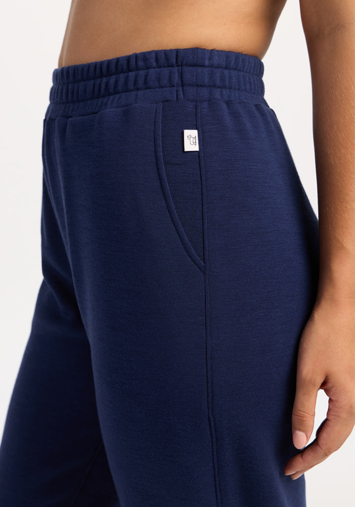 Woman in Woolx Parker Sweatpants - Ocean Cavern, with elastic waist, stands relaxed in stylish navy joggers.