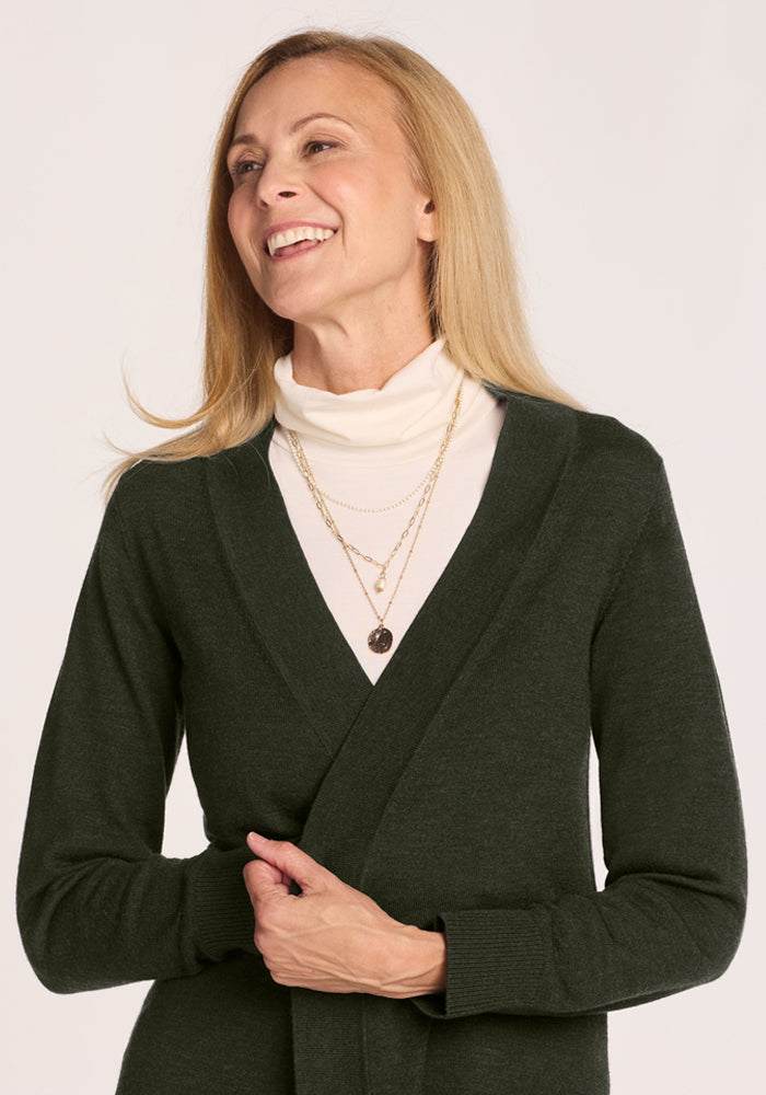 Smiling woman in the Woolx Macie Sweater - Duffel Bag, white turtleneck, and layered necklaces against a plain backdrop.