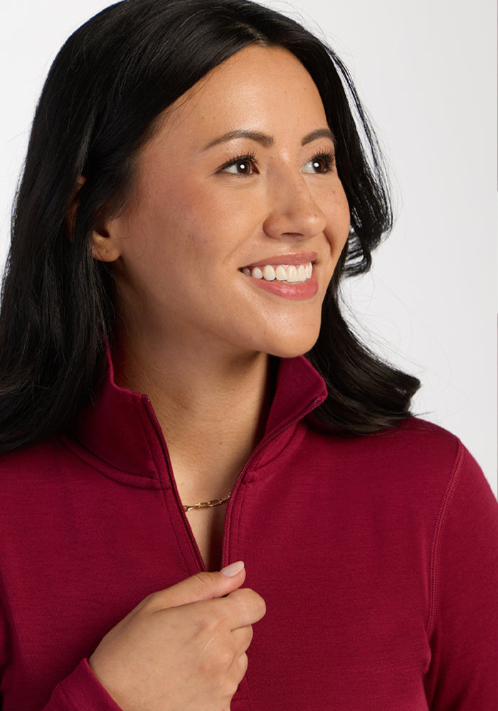 Woman with long dark hair smiles, wearing the Woolx Brooke 1/4 Zip in Beet Red and a gold chain necklace.