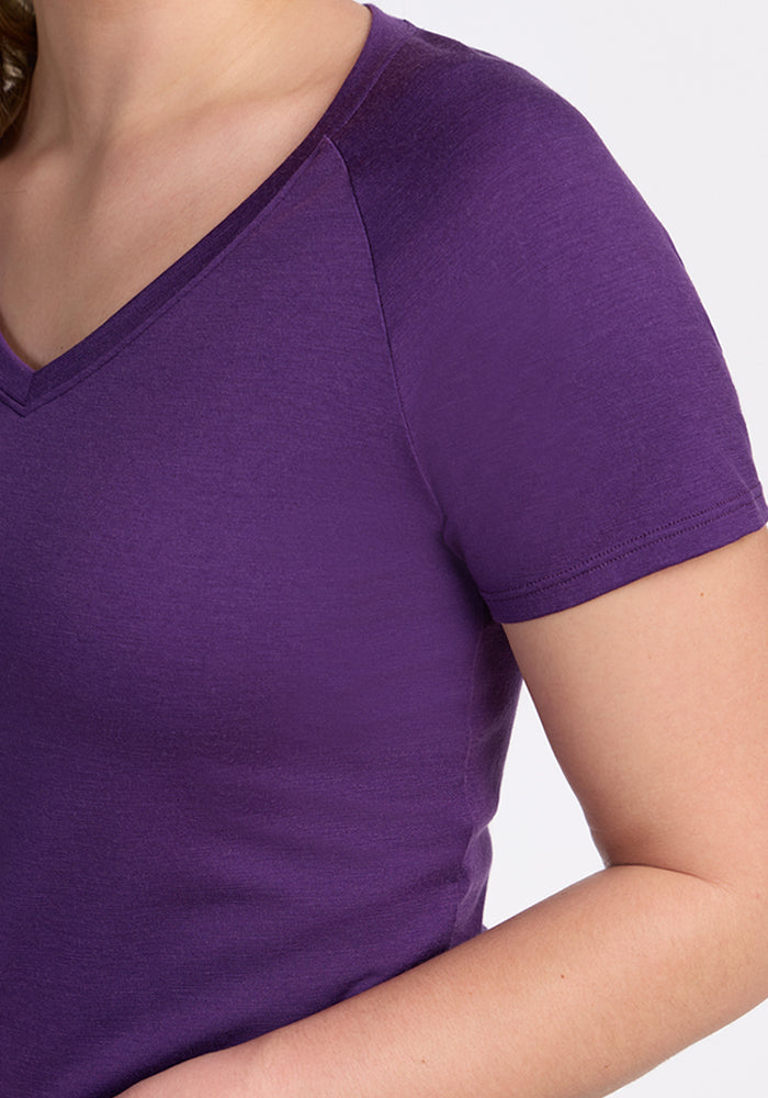 A person is shown from shoulders to waist wearing the Woolx Mia V Neck in Plum Crush, a short-sleeved Merino wool travel tee, with their left arm relaxed at their side.