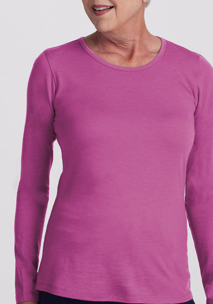 An older woman wears the Woolx Remi Long Sleeve T-Shirt in Purple Wine. Seen from shoulders to hips, she smiles softly, while the odor-resistant merino wool fabric stands out against a plain, light background.