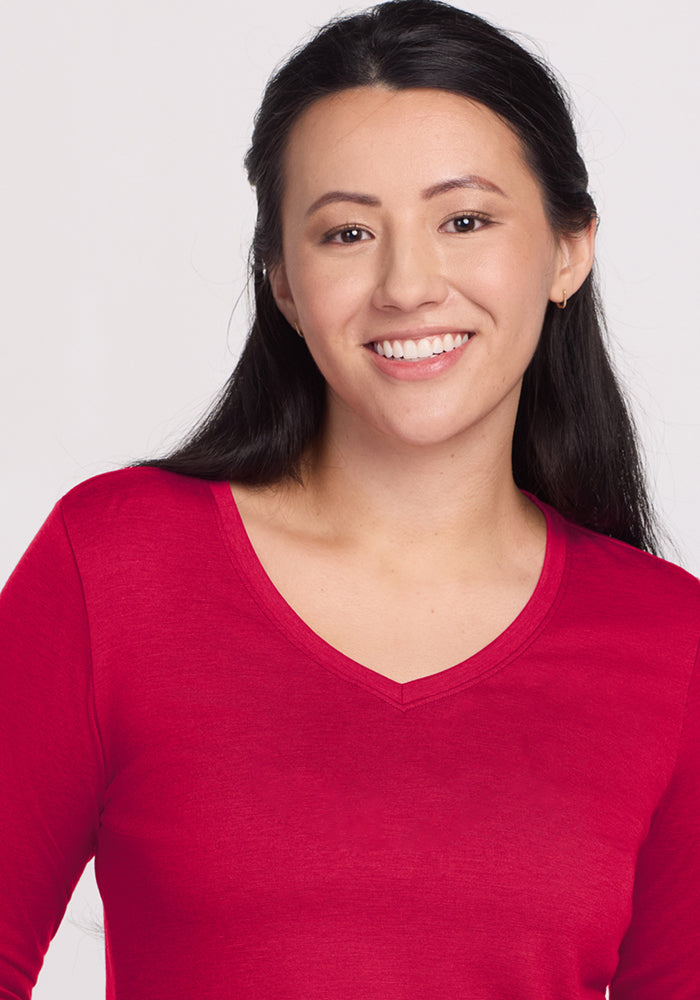 A woman with long dark hair, wearing the Woolx Millie Long Sleeve in Poppy Spark, smiles at the camera against a plain light background.
