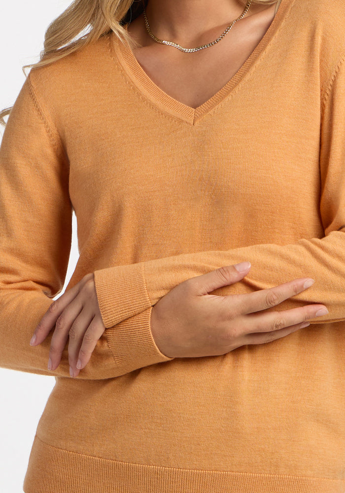 Person in a Woolx Francesca Sweater - Butterscotch, arms crossed, chain necklace; only torso and arms shown.
