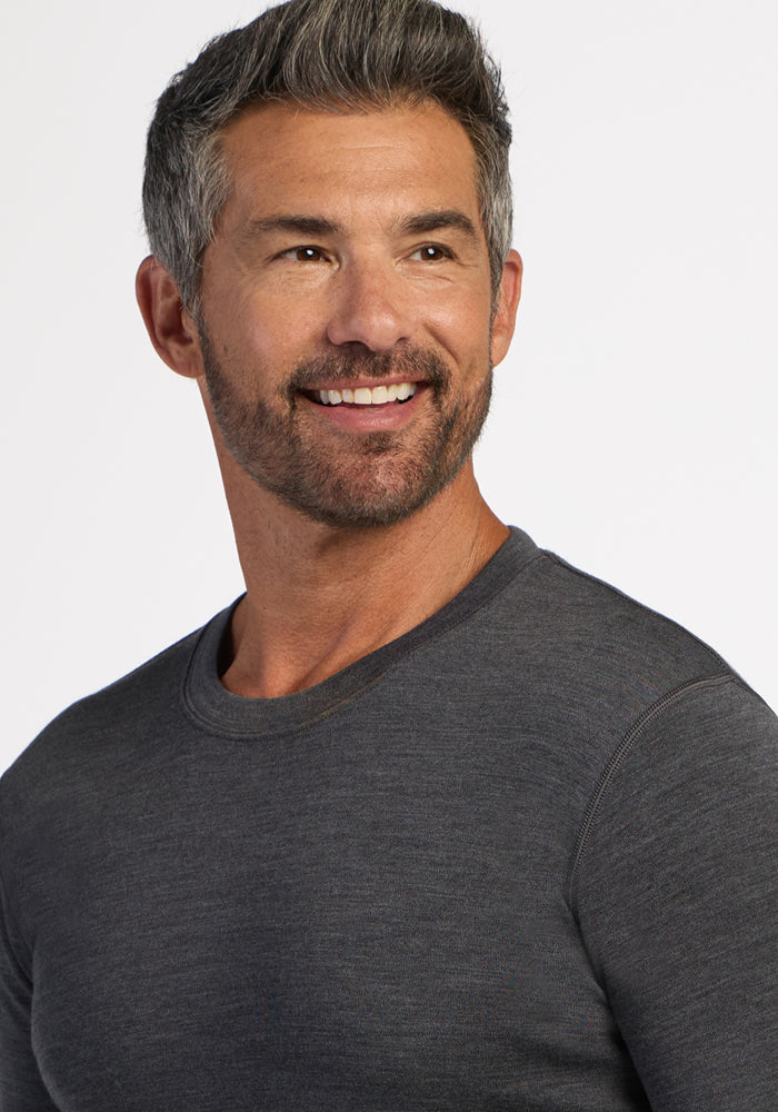 Smiling man in Woolx Explorer Base Layer - Cinder Melange; short salt-and-pepper hair, light background.