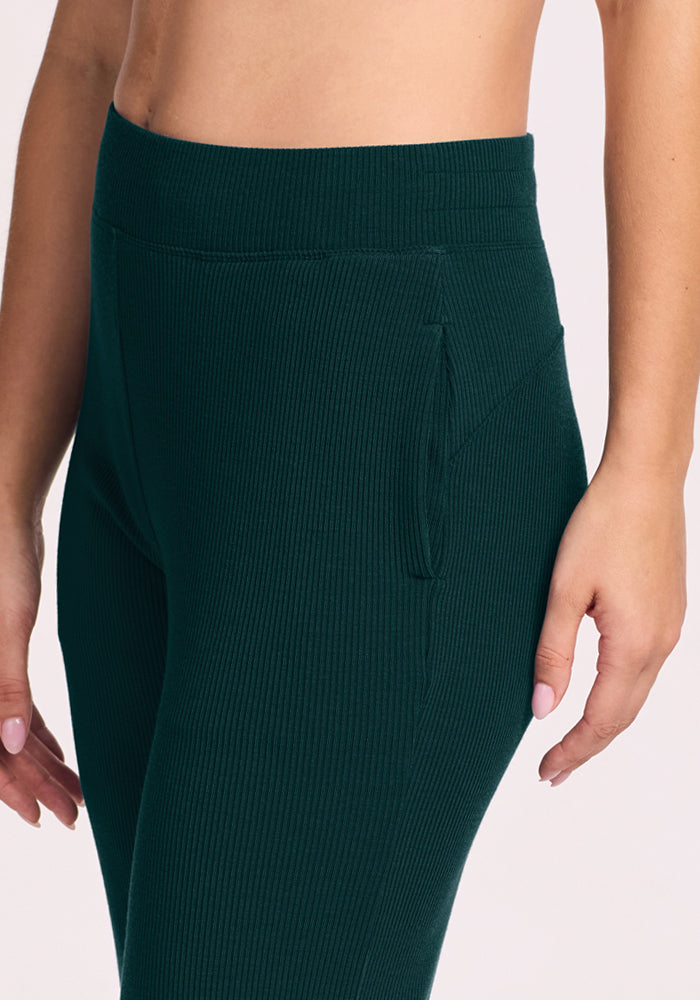 Someone in Woolx Luca Ribbed Pants - Deep Pine, high-waisted with side pockets, shown waist to mid-thigh.