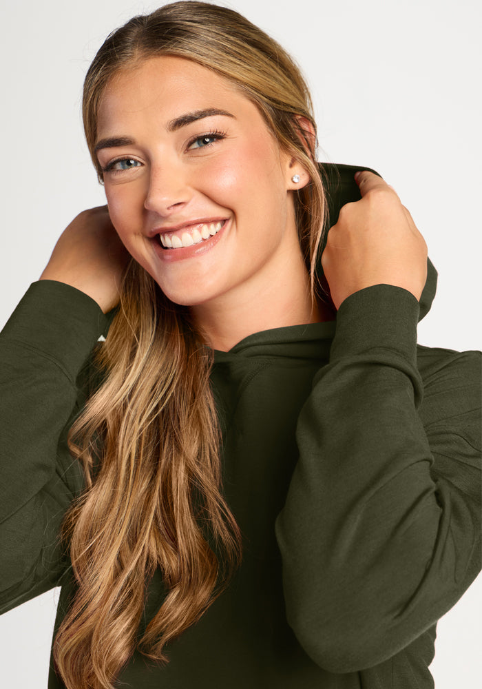 Smiling woman with long blonde hair adjusts the Woolx Lizzy Hoodie - Everleaf hood against a plain backdrop.