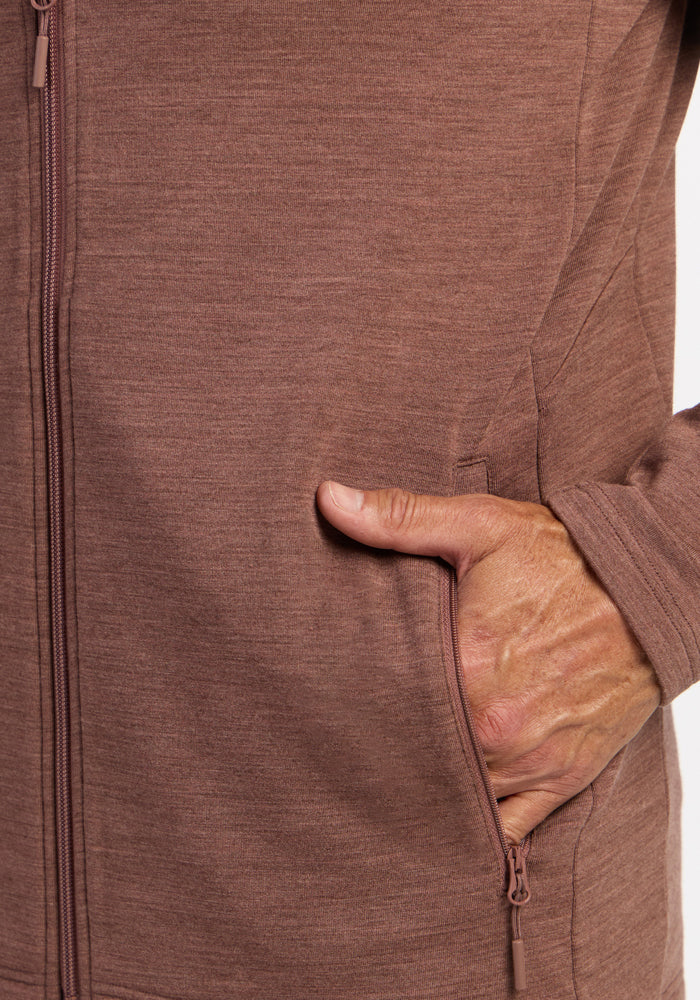A hand is partially tucked into the pocket of a Woolx Boulder Hoodie - Sable Heather.
