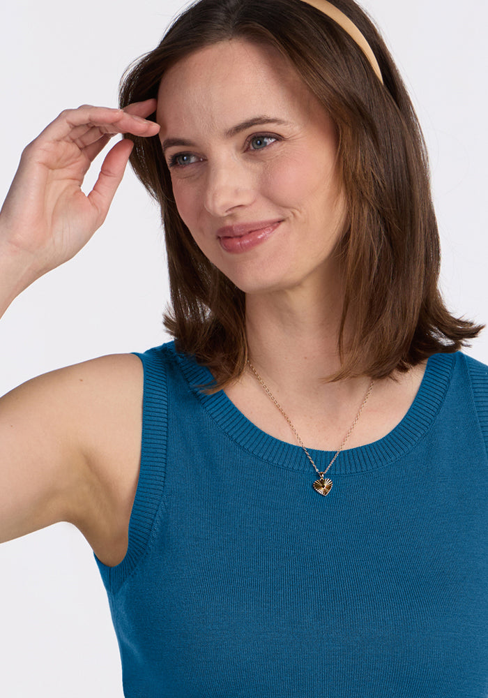 Smiling woman in a blue Woolx Chessy Tank Top, gold necklace, beige headband, and brown hair.