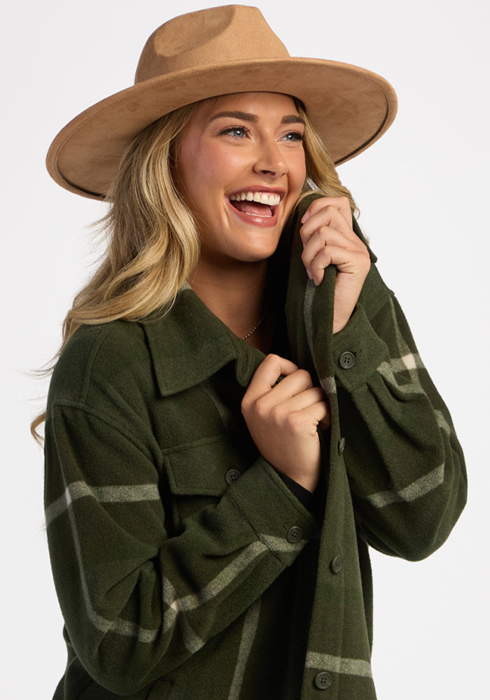 Smiling woman in a tan hat and Woolx Sawyer Shacket - Driftwood Fern Plaid, holding her collar against a white background.