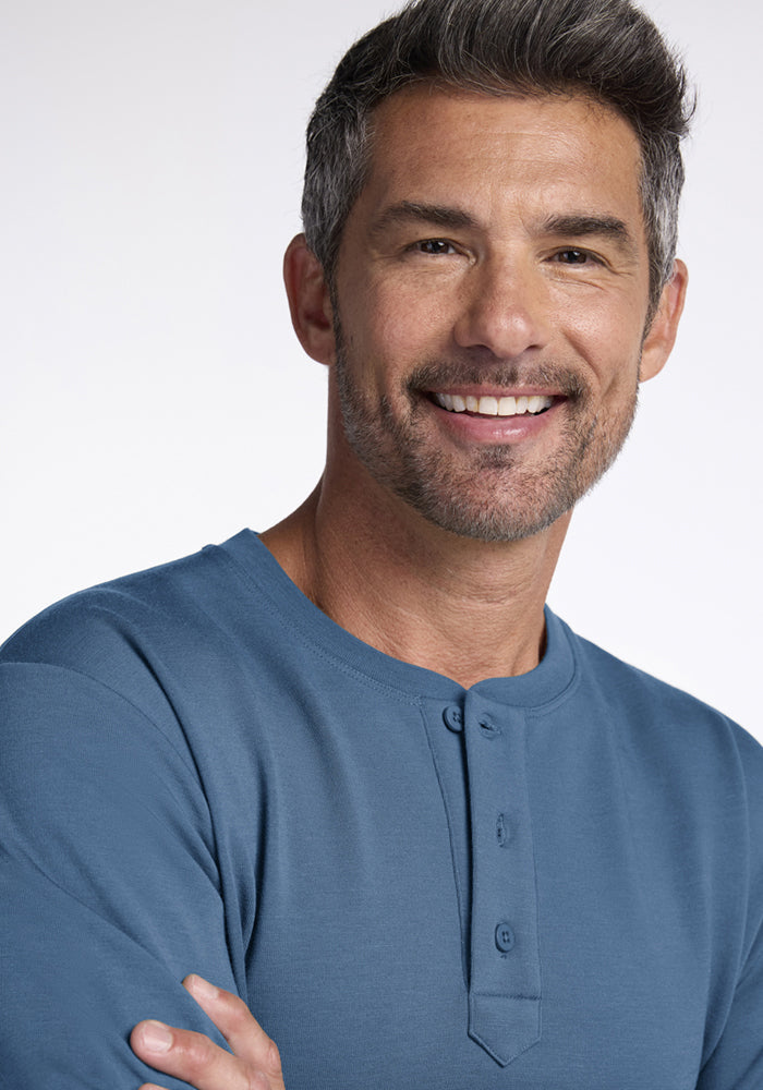 Smiling man in a blue Woolx Jackson Henley - Blue Ashes stands against a light background.