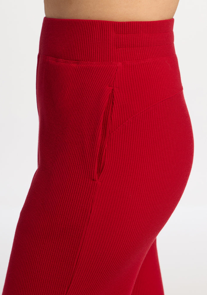 Close-up of a person wearing Woolx Luca Ribbed Pants in Maraschino Cherry, featuring hip pocket and seam details.