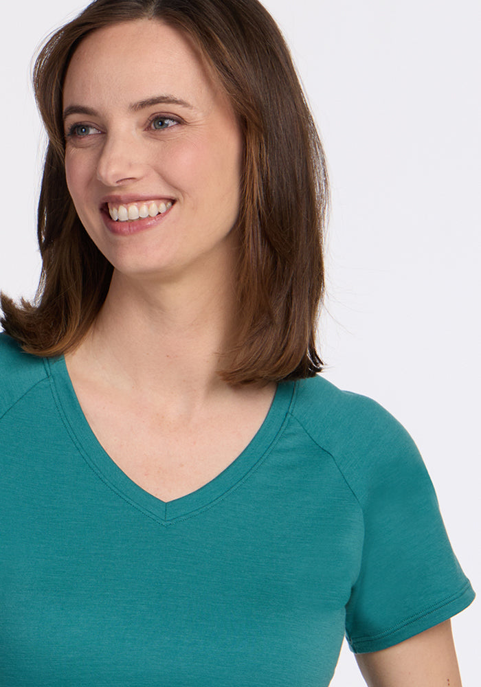 A woman with shoulder-length brown hair smiles while looking to the side, wearing the Woolx Mia V Neck - Surfside women’s Merino wool tee against a plain white background.