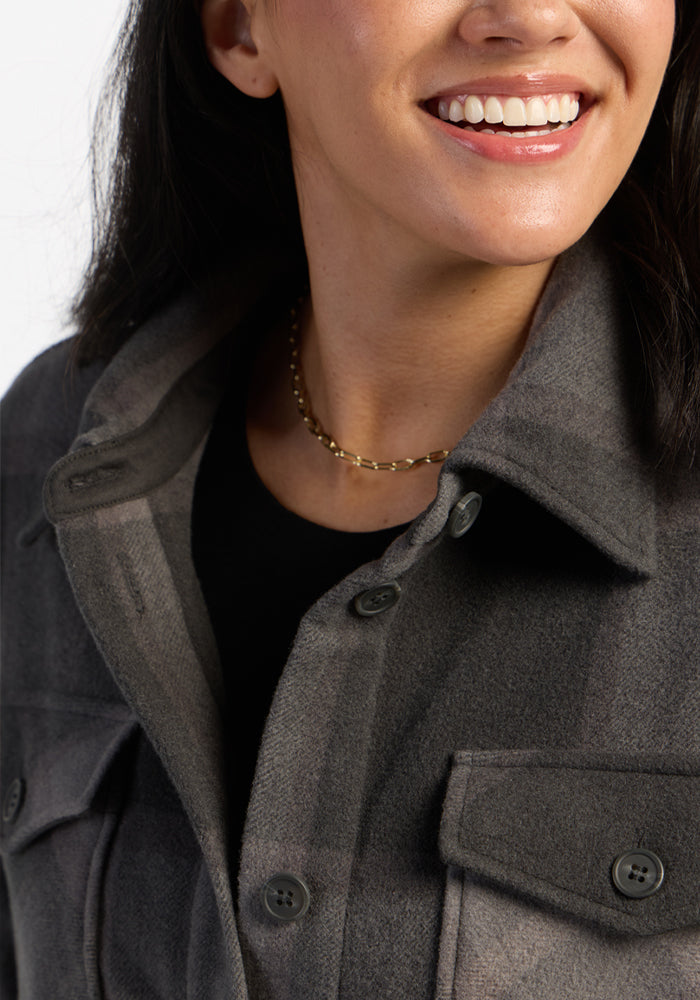 Woman smiling, wearing the Woolx Sawyer Shacket in Volcanic Ash Plaid, a black shirt, and a gold chain necklace.