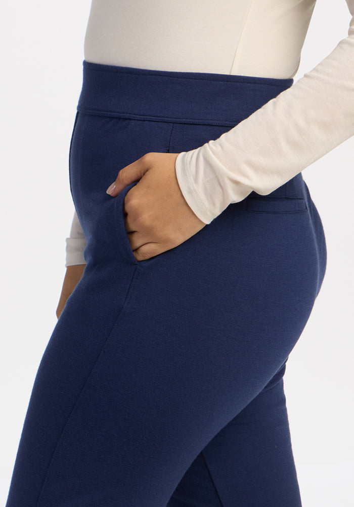 Person wears Woolx Emerson Straight Leg Pants Petite in Ocean Cavern with a cream long-sleeve top, hand in pocket.
