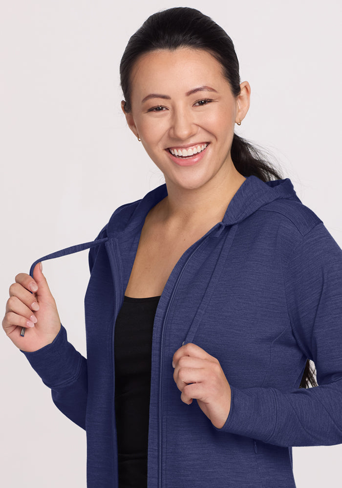 Smiling woman in the Woolx Ryann Hoodie - Twilight Storm, holding drawstrings—your go-to travel essential.