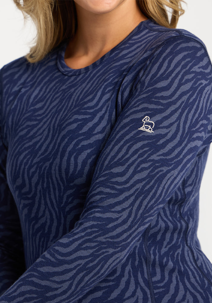 Woman wears Woolx Maddie Baselayer Top in Midnight Safari, featuring a zebra print and small white sleeve logo.