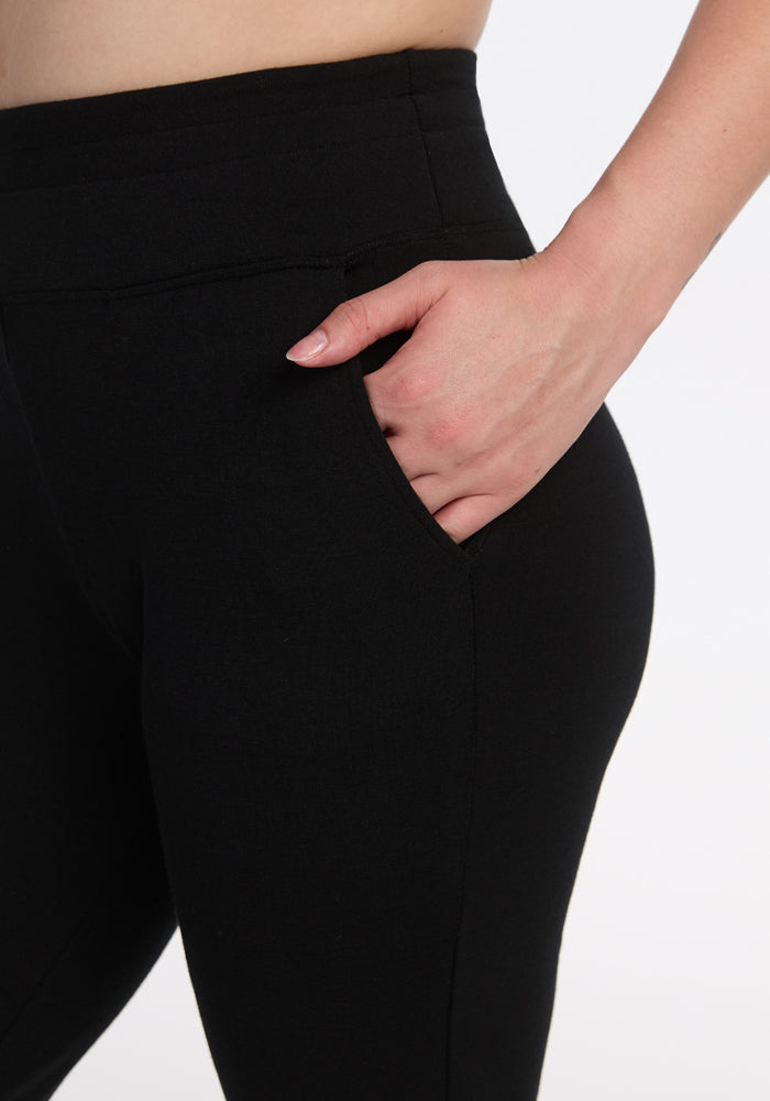 A close-up of a person wearing Woolx Madden Joggers - Black with their right hand in the side pocket, highlighting the hip and upper thigh area against a white background.