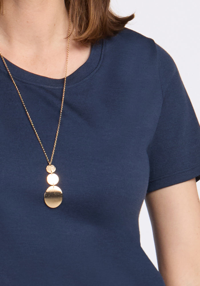 A person wears the Woolx Georgie Dress in Deep Navy, styled with a long gold necklace featuring three round, reflective pendants. Only the upper torso and part of the necklace are visible.