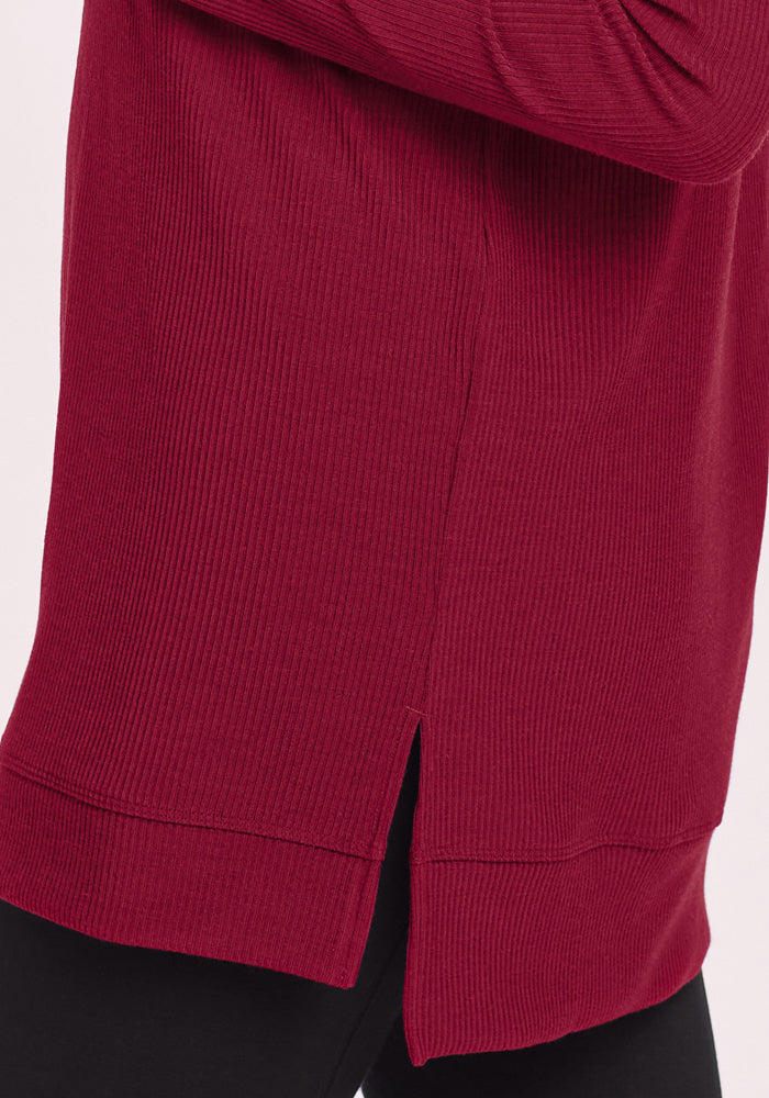 Close-up of the Woolx Evie Petite Tunic in Beet Red, featuring ribbed merino wool and a side slit, styled with black pants.