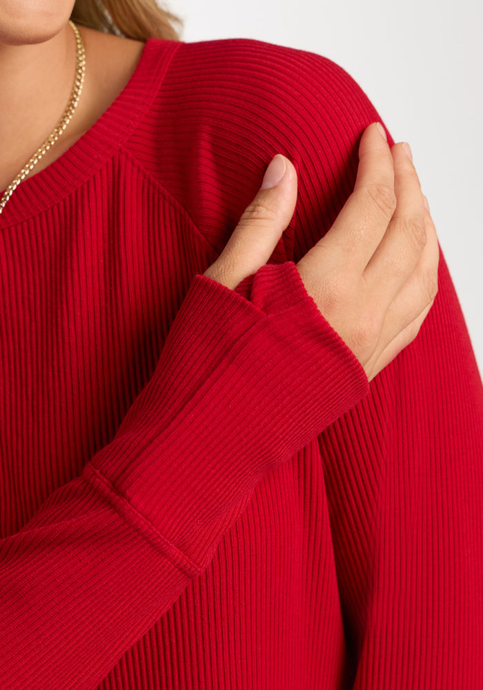 A woman in the Woolx Ainsley Sweater—Maraschino Cherry—touches her shoulder with her left hand.