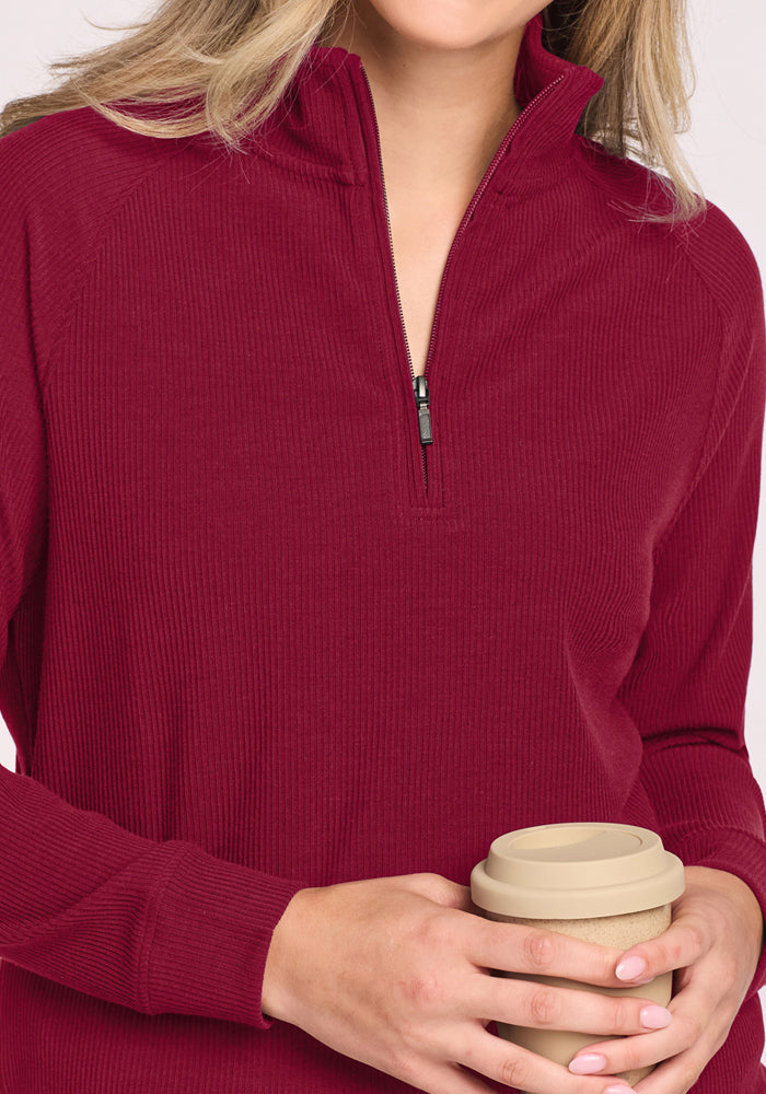A person in a Woolx Quinn Ribbed 1/4 Zip - Beet Red holds a reusable coffee cup from shoulders to mid-torso.