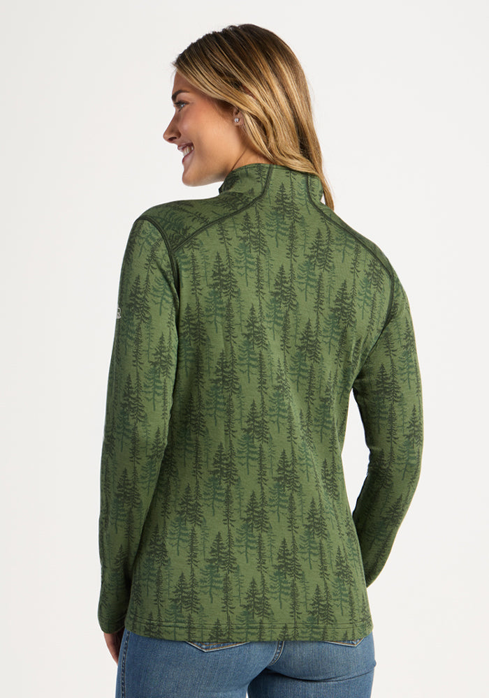 Smiling woman in Woolx Emi 1/4 Zip - Forest Friends, a green, tree-print Merino wool top, paired with blue jeans.