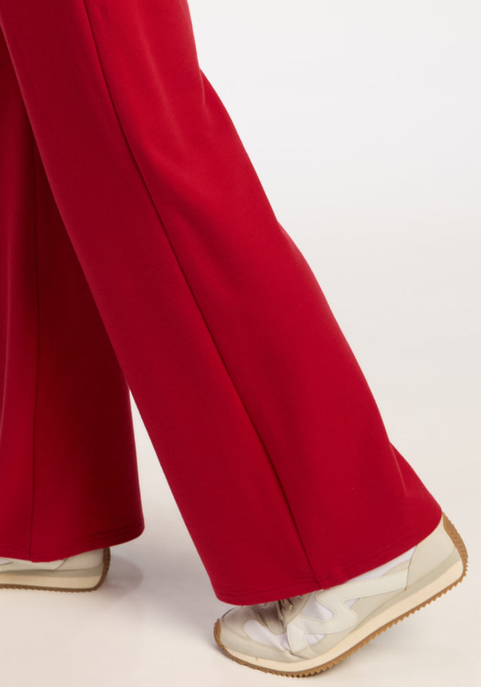Model in Woolx Eloise Wide Leg Pants in Maraschino Cherry and white sneakers stands, highlighting a relaxed look.
