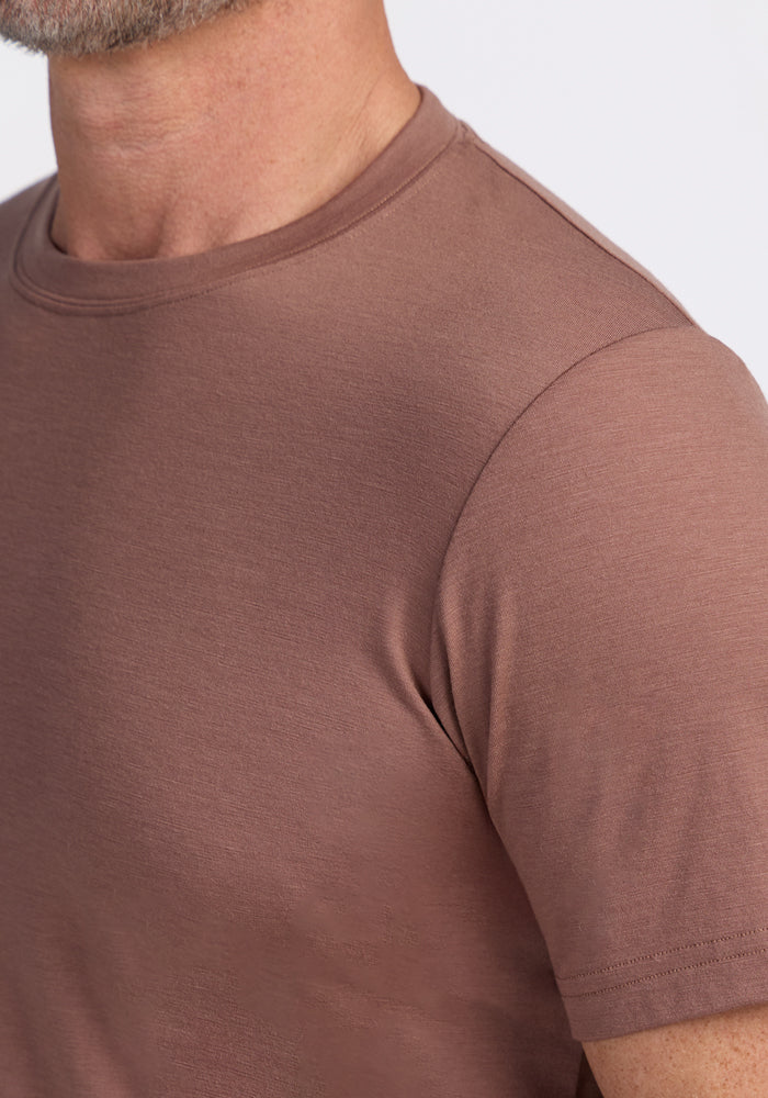 Close-up of a person wearing the Woolx Endurance Tee in Sienna Kiss, highlighting the shoulder, sleeve, neck, and chin against a plain light background.