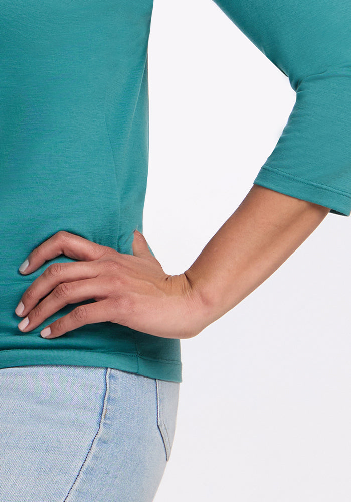 A person wears the Woolx Jenny 3/4 Sleeve Crew Neck in Surfside with light blue jeans, standing against a plain white background with one hand on their hip.