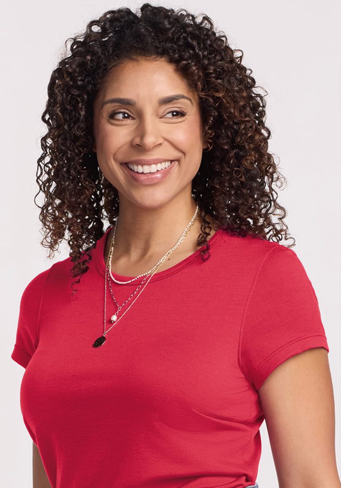 Woman with curly hair smiles, wearing Woolx Addie Crew Neck - Berry Ice Pop, against a plain light background.