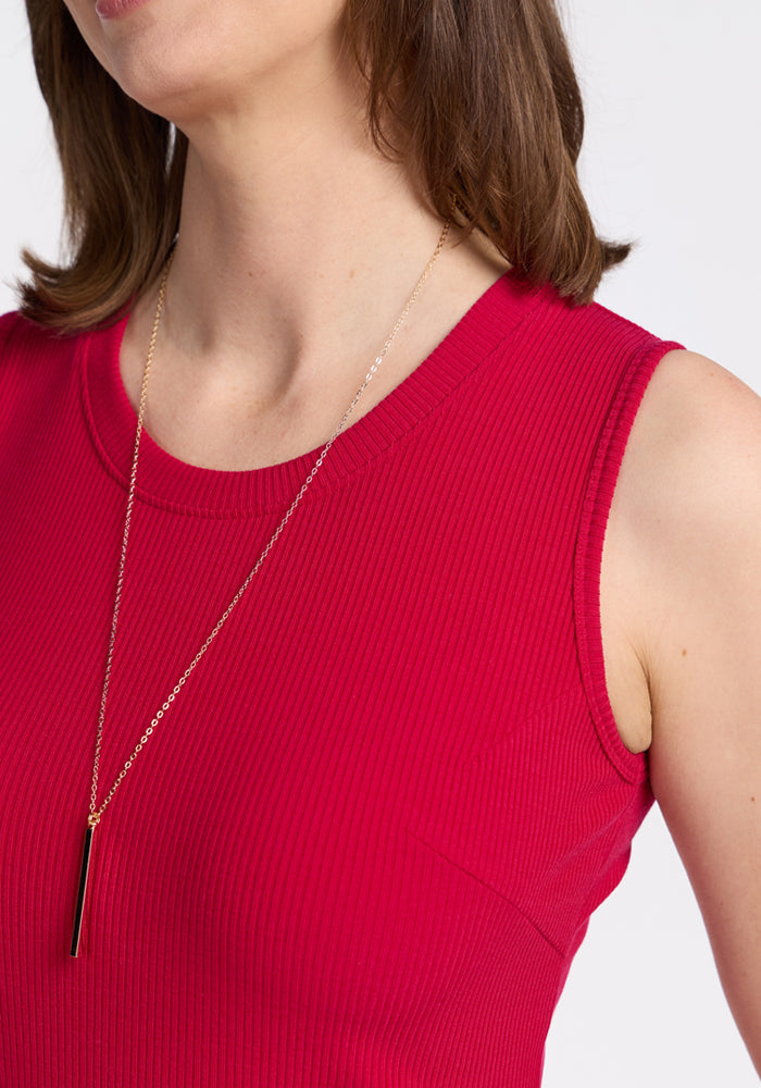A woman wears the Woolx Iris Ribbed Dress in Poppy Spark, paired with a gold necklace featuring a black pendant. She is photographed from the shoulders up against a white background.