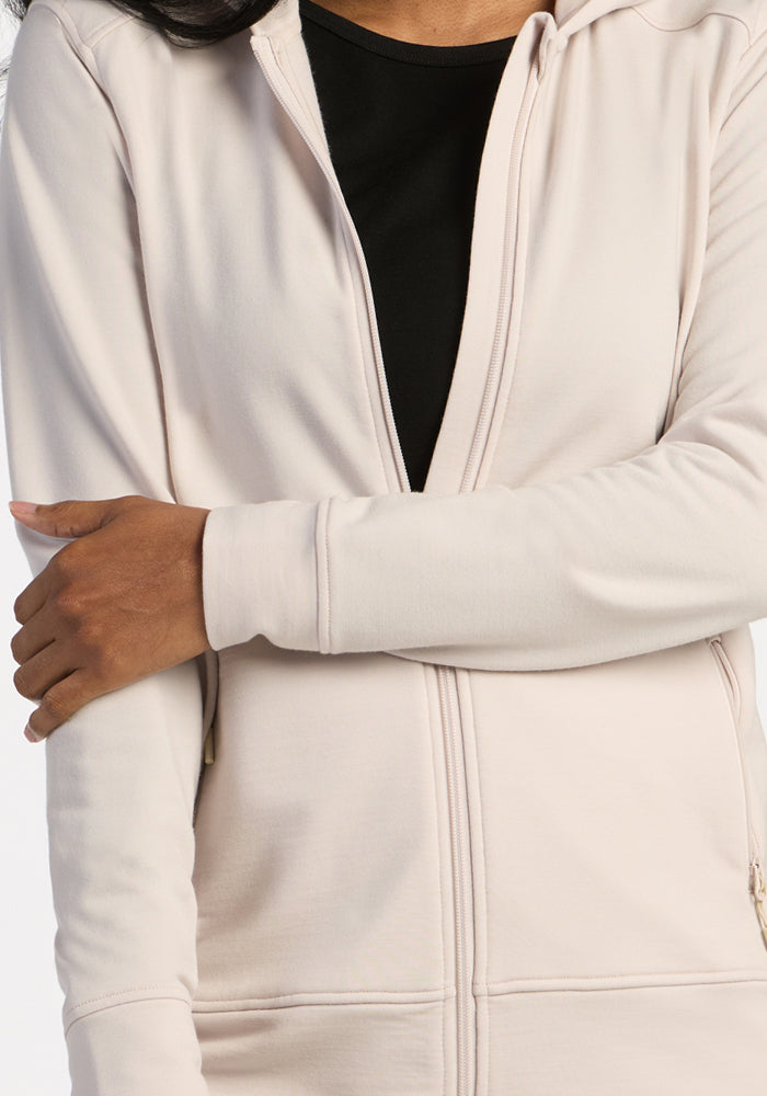 A person in the Woolx Darby Zip Up Hoodie - Ecru over a black shirt crosses their arm across their body.