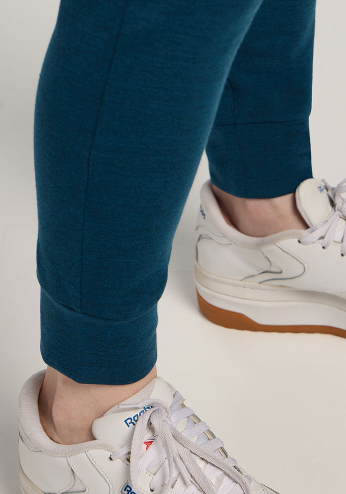 Close-up of a person wearing Woolx Madden Petite Joggers in Majolica Blue and white Reebok sneakers on a light surface.