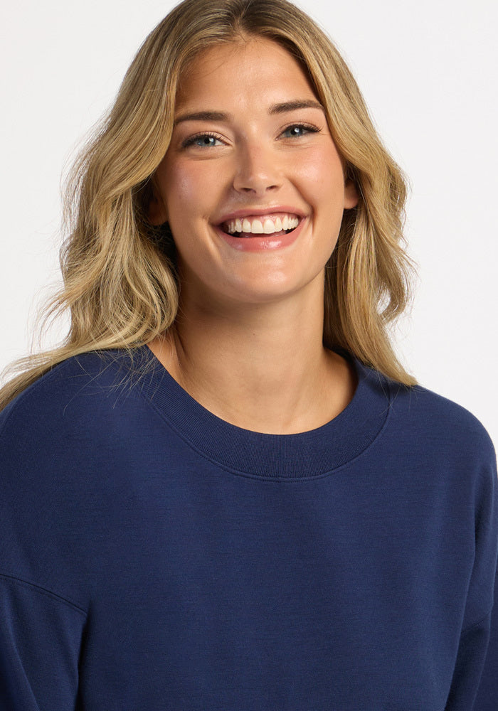 A smiling woman wearing a dark blue, moisture-wicking Molly Crewneck - Ocean Cavern merino wool sweater.