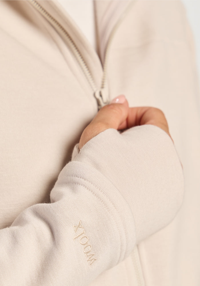 Close-up of a light beige Woolx Cubby Hooded Sweatshirt - Ecru with a zip-up front and thumbhole cuffs.