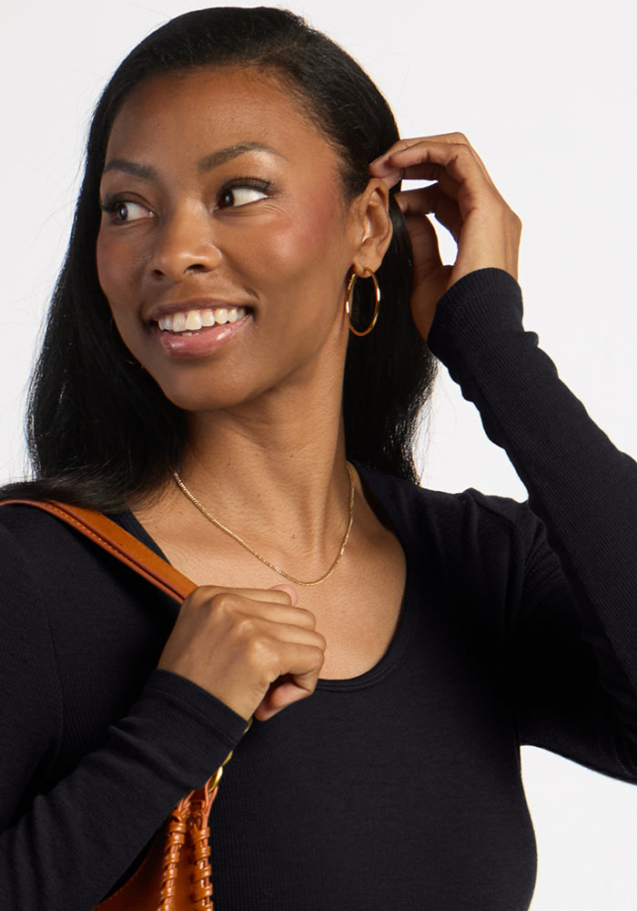 Woman smiling in the Woolx Katie Ribbed Long Sleeve - Black, gold hoops, necklace, and a brown bag on her shoulder.