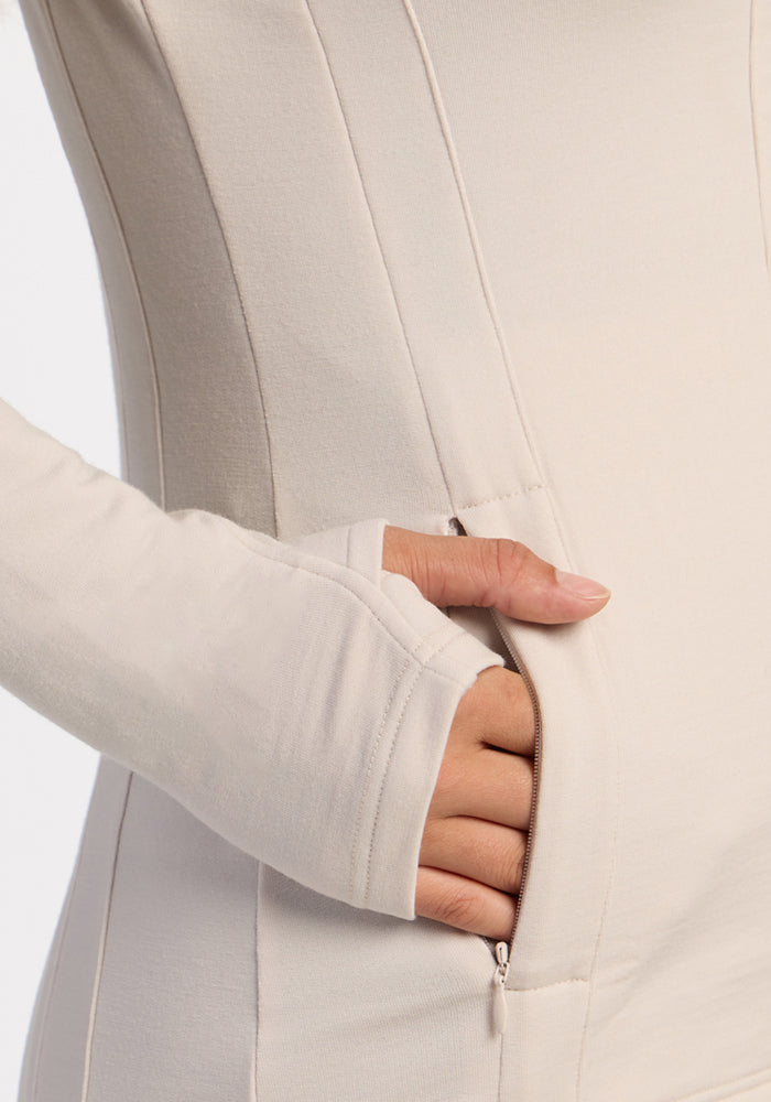 A thumbhole sleeve hand rests in the pocket of a Woolx Finley Zip Up Sweatshirt - Ecru, odor-resistant fabric.