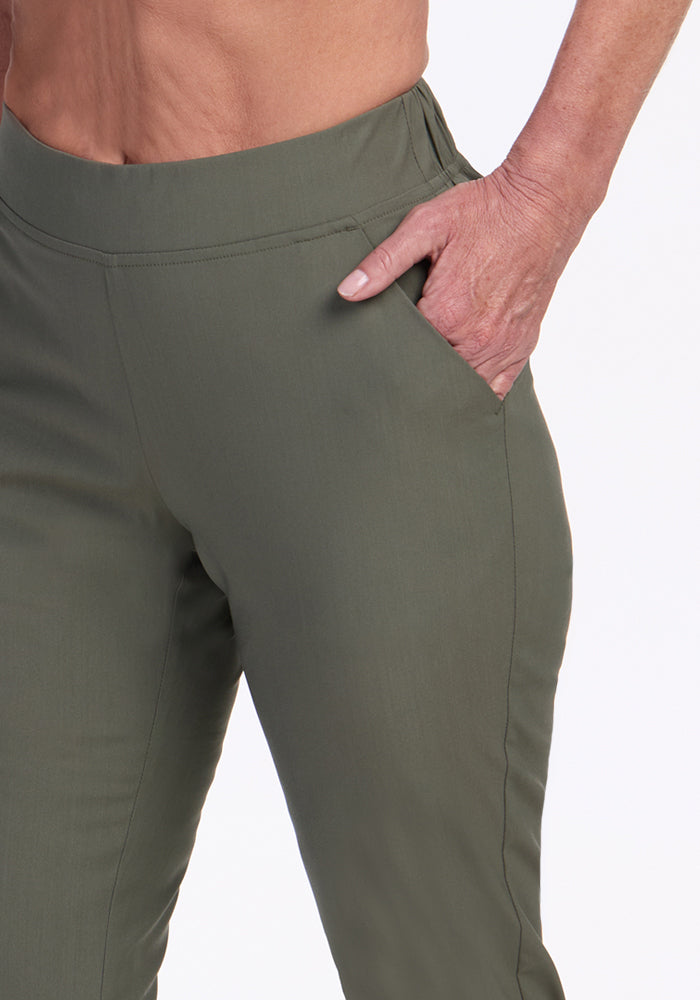 A person wearing Woolx Nicole Ankle Pants in Sage Olive stands with one hand in their pocket, offering a close-up view from waist to thigh against a plain background.