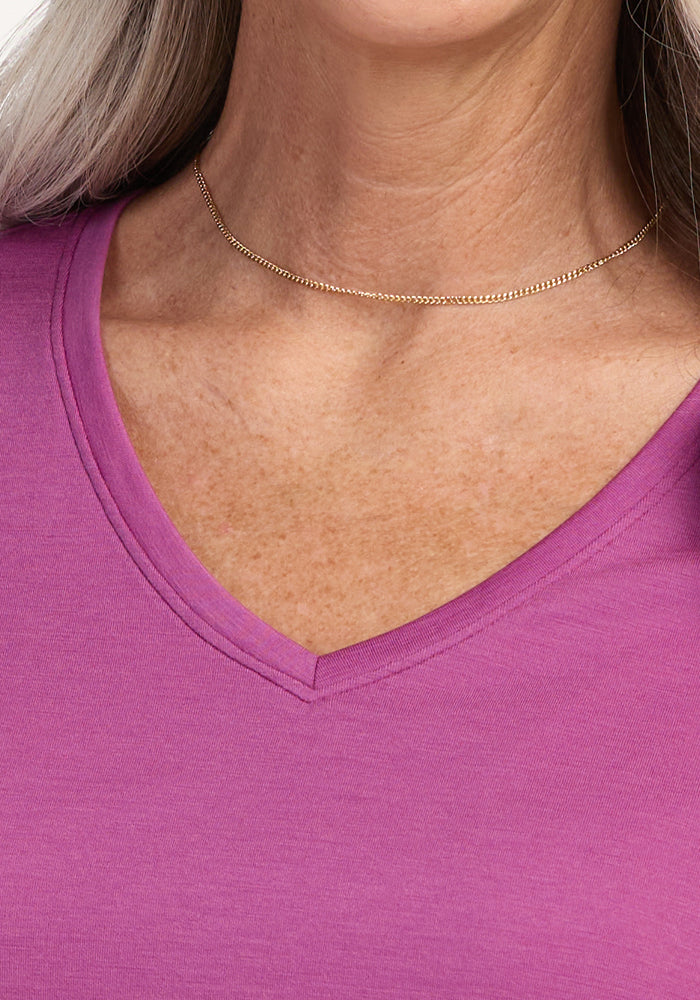 A close-up showcases a person wearing a simple gold chain and the Woolx Junie V Neck in Purple Wine, a women’s relaxed-fit Merino wool tee, highlighting the neck, collarbone, and shoulder.