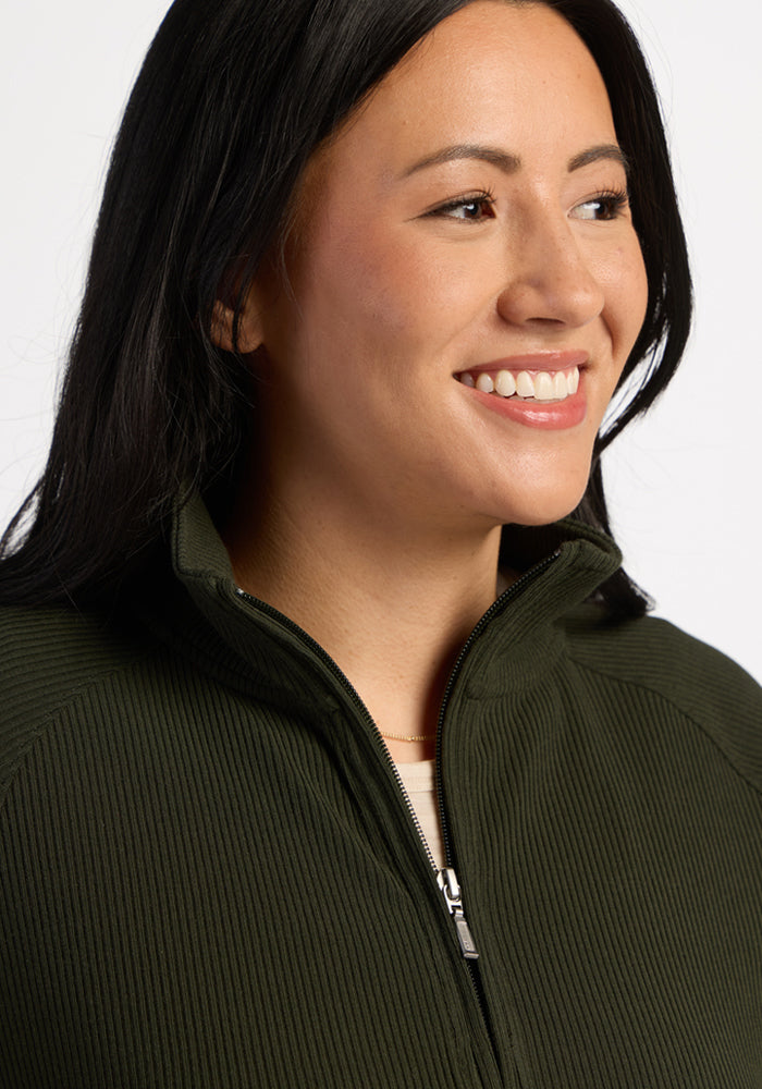 Woman with long dark hair smiles, wearing the Woolx Quinn Ribbed 1/4 Zip - Duffel Bag against a plain background.