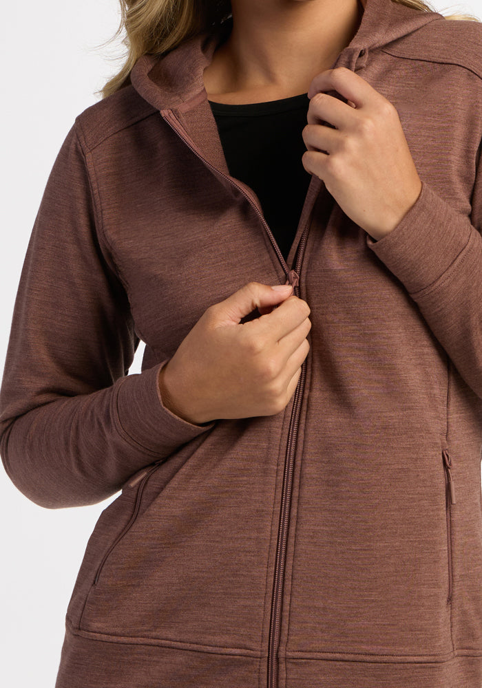 Model in Woolx Darby Zip Up Hoodie in Sable Heather, partially unzipped over a black top, plain background.