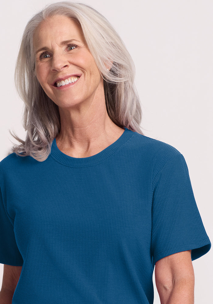 Smiling older woman with long gray hair wears the Woolx Delia Ribbed Short Sleeve in Moroccan Blue, standing against a light background.